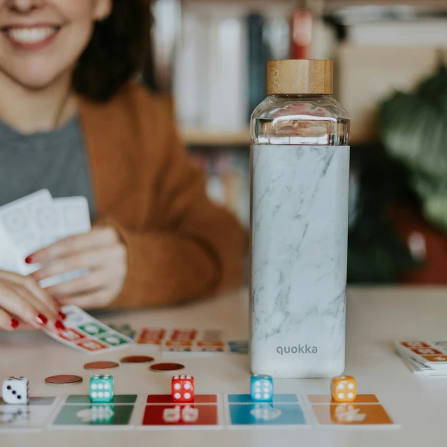 a woman in a brown jacket sitting at a table with two dice and a bottle