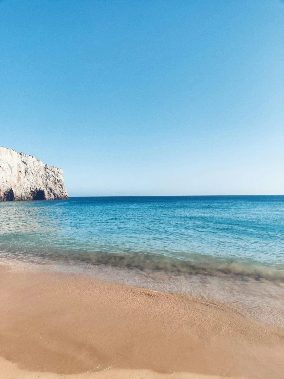 a blue ocean and rock face on a beach