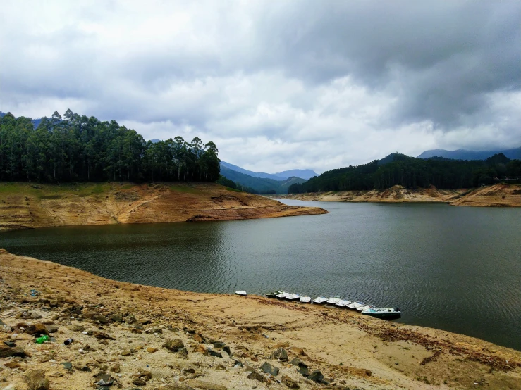 a lake with boats on the bank next to it and a mountain behind