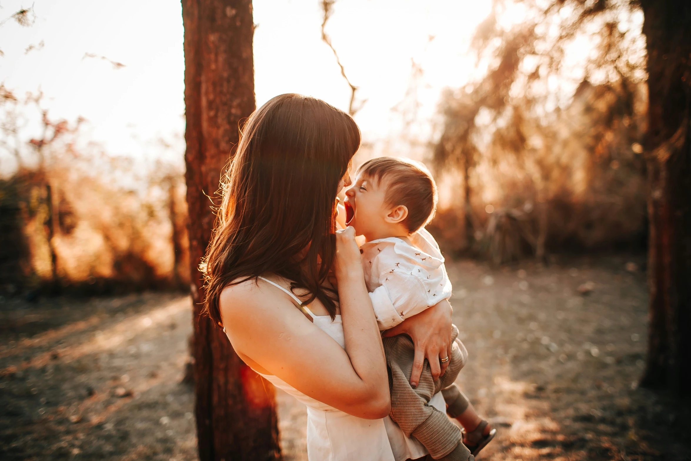 a woman holding a baby in her hands while standing next to trees