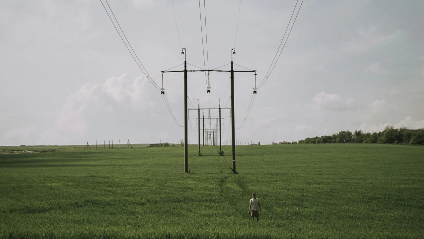 a woman in the middle of a field with power lines on top of it