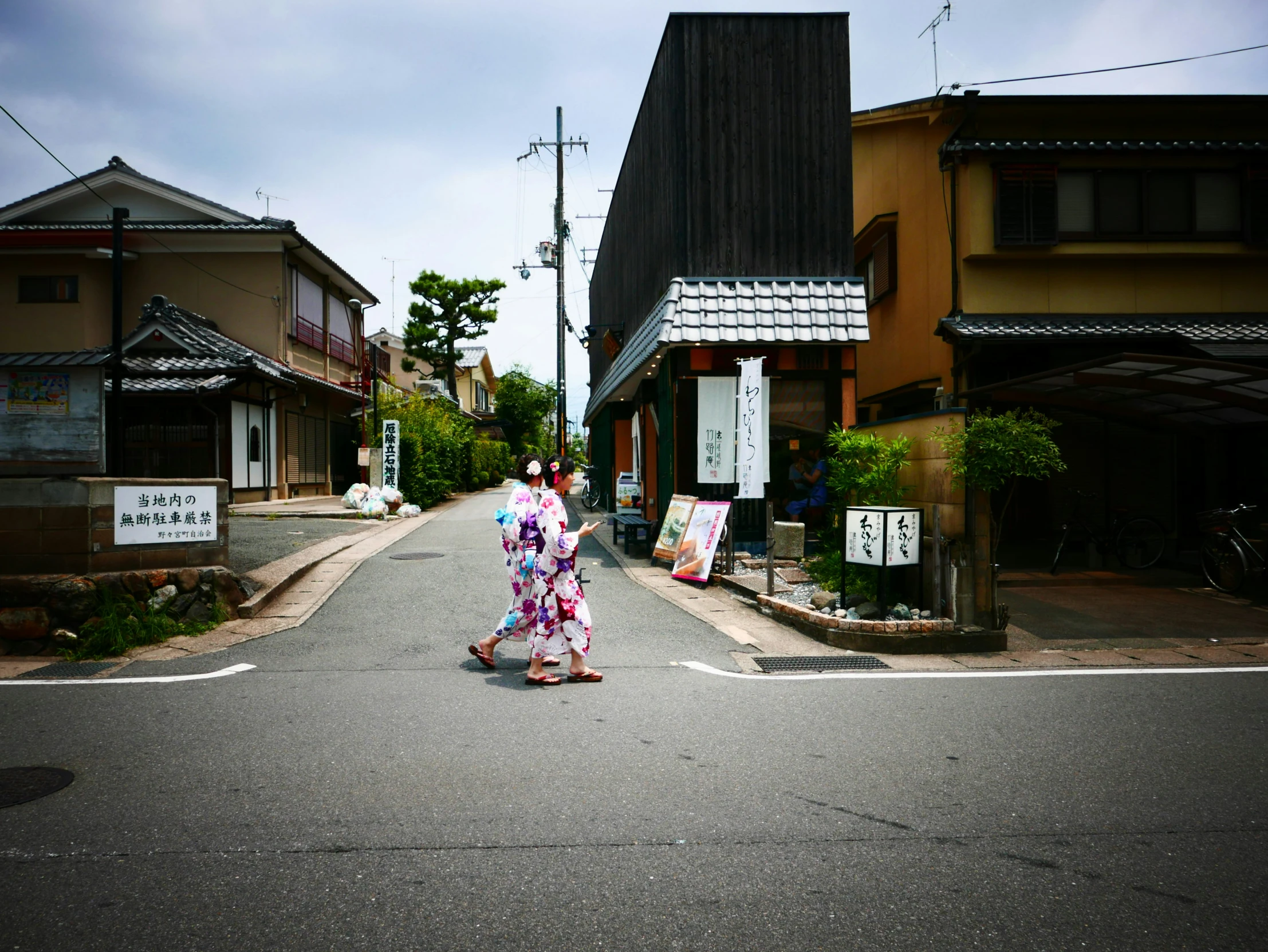 two woman crossing the street on a street with buildings