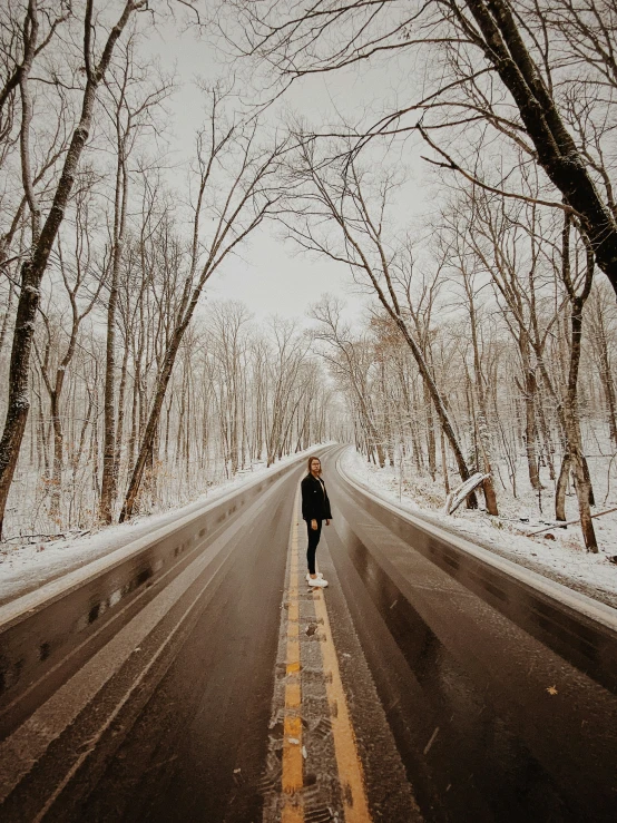 person walking down snowy road between tall trees