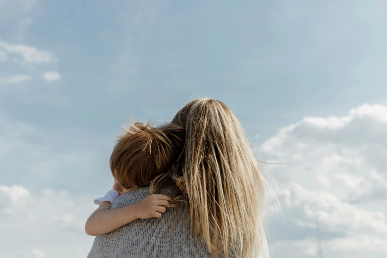 a woman with a baby wrapped in her arms, against a blue sky