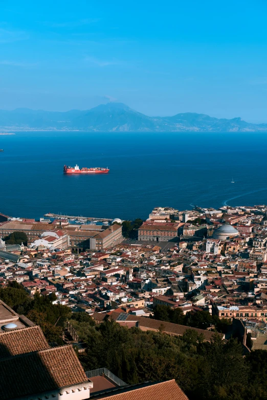 a view from a hill looking at the sea with buildings in front