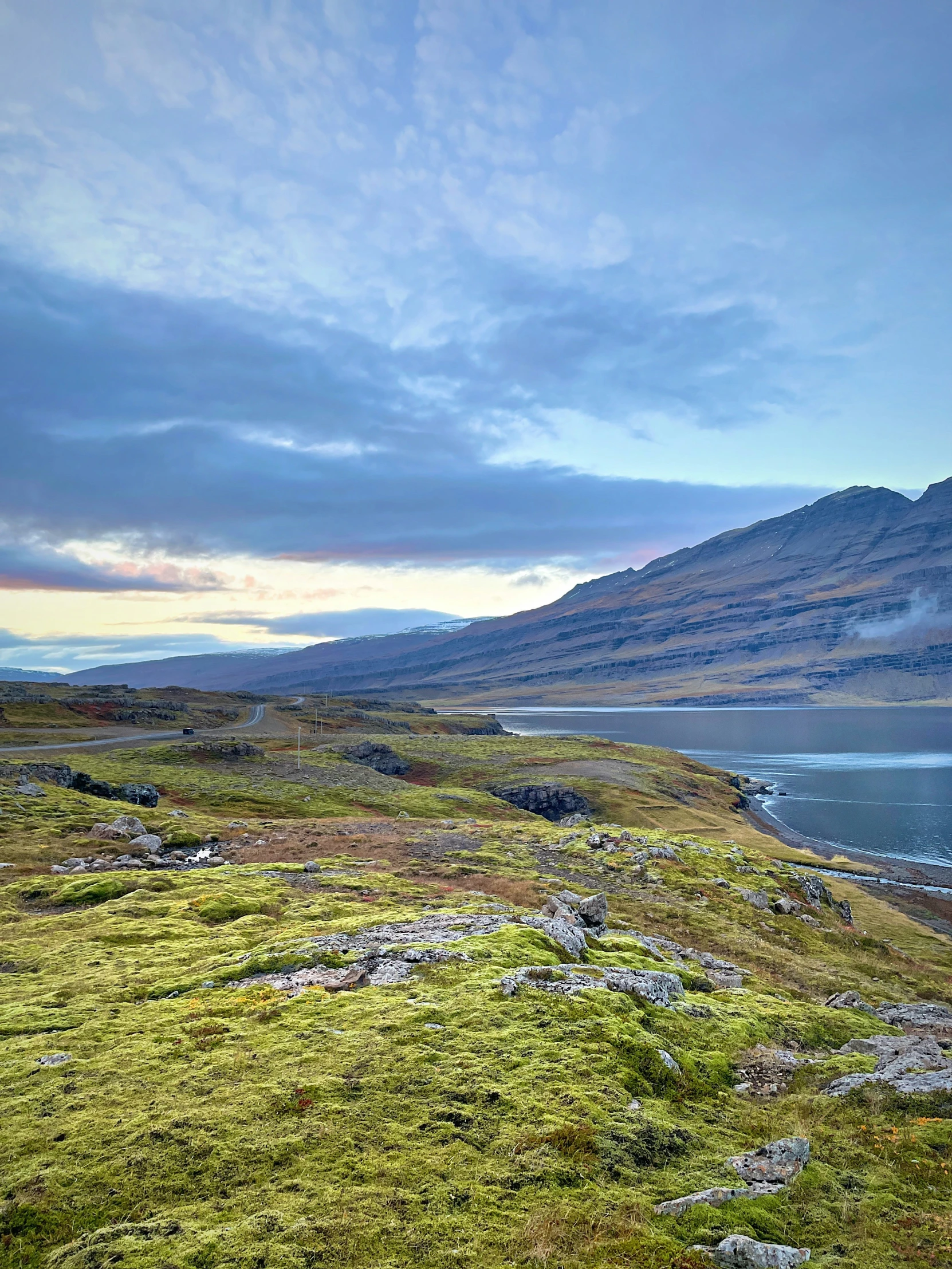 a grassy hill with rocks on it with water and a mountain in the background