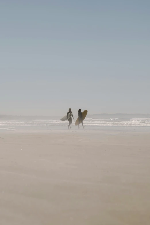 people walking along the beach while carrying surfboards