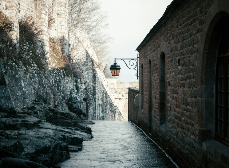 an alley leading to a dark stone wall and street lamp