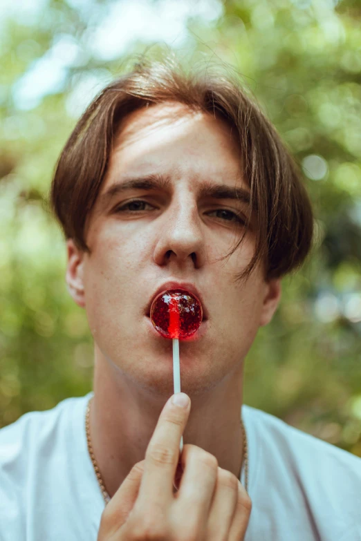 a boy making a serious face and holding a red lollipop up to his mouth