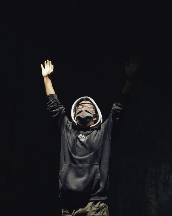 the person wearing a mask and jacket raises their hands