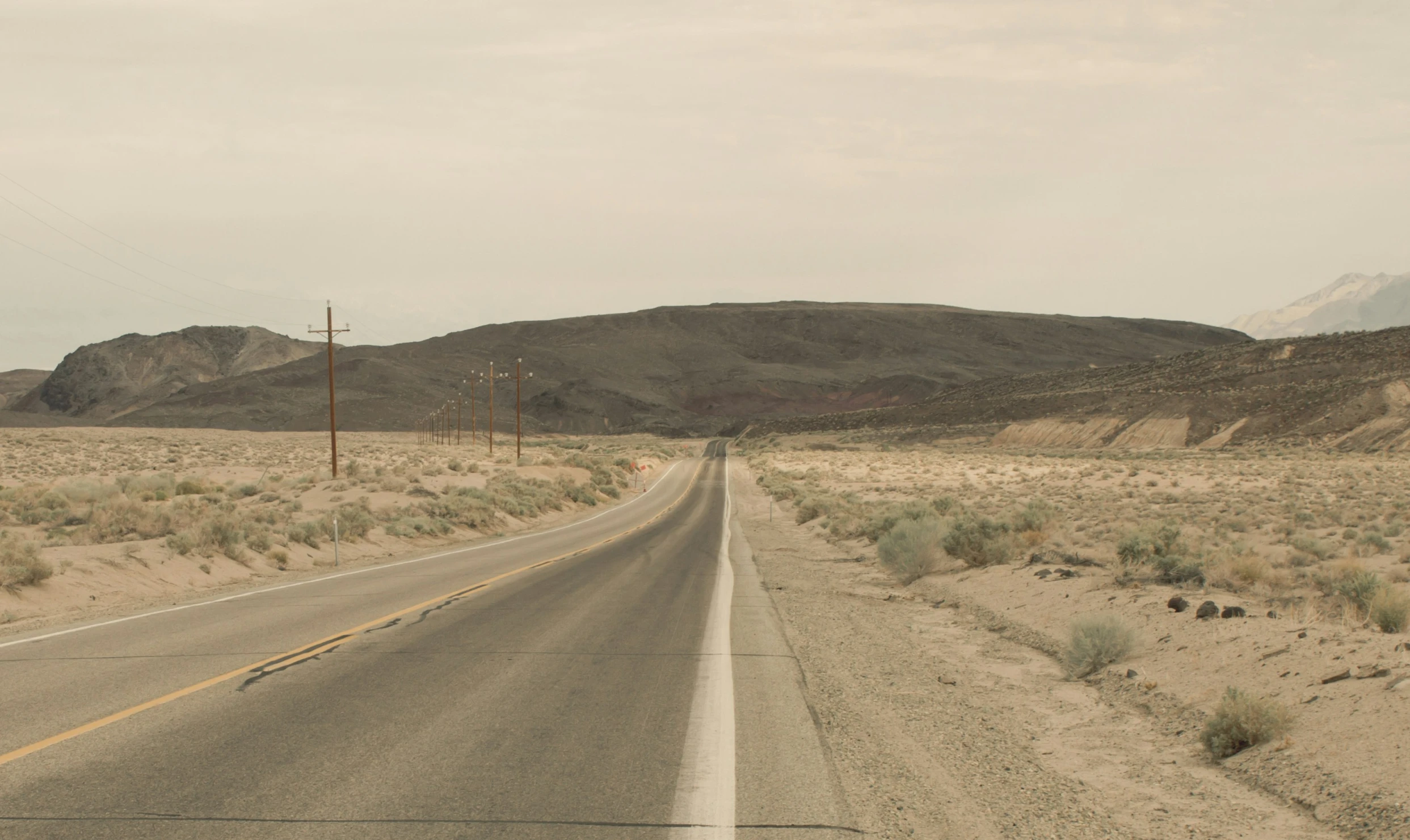 a road and hills in the desert with power lines in the background