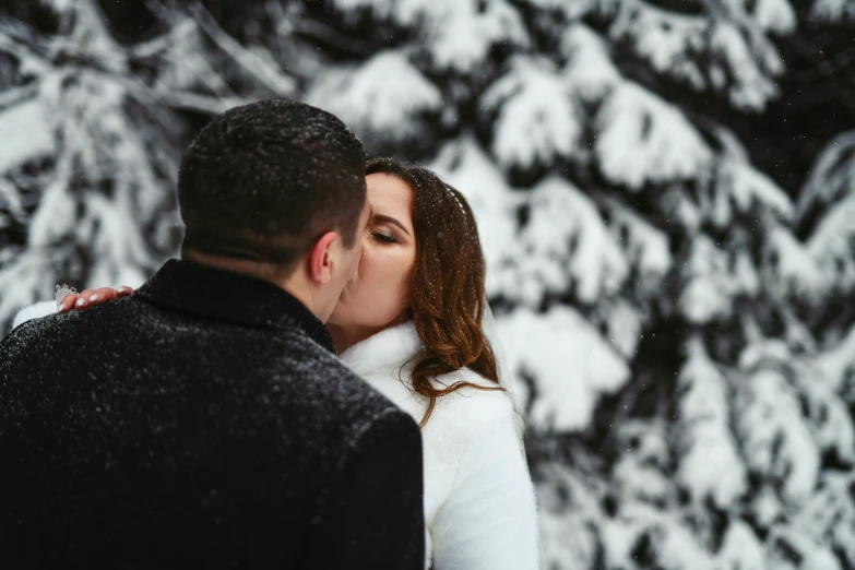 a man and woman are standing in front of a snow covered tree