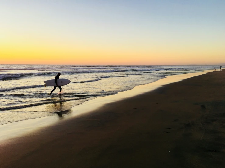 person carrying surf board on beach at sunset