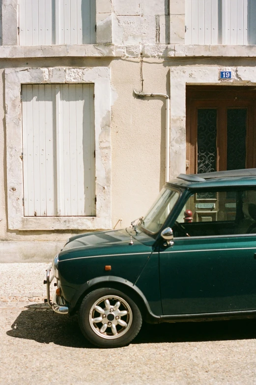 a green small car sits parked in front of a white building