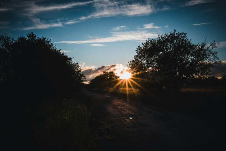 the sun is setting over a dirt path