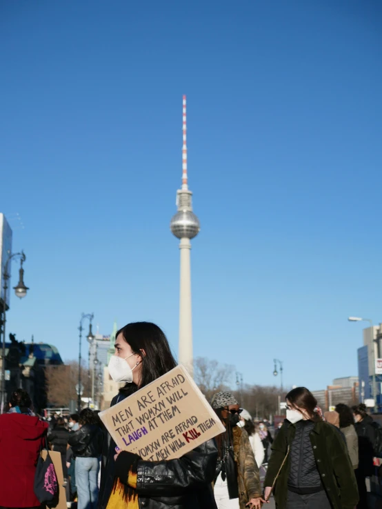 woman holds sign in front of television tower
