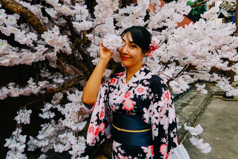 the asian girl is posing for the camera by her blooming tree