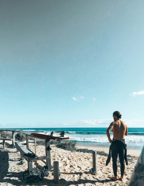 man standing on sandy beach with board and surfboard