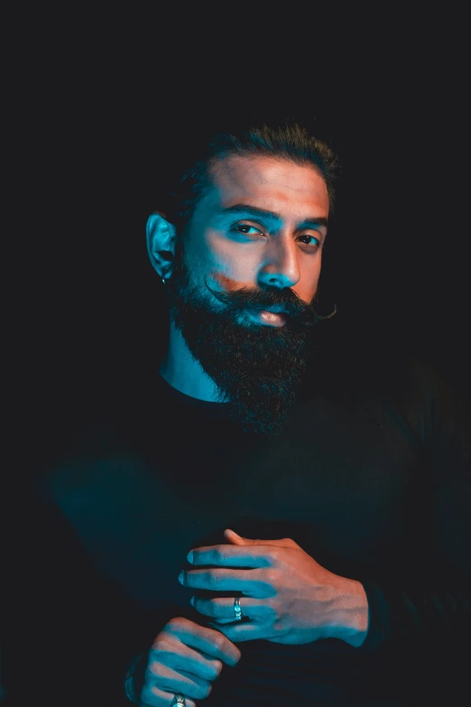 a bearded man in a black sweater is standing in the dark