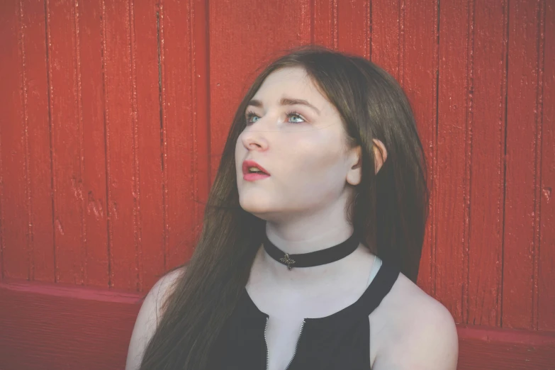 a girl with long hair wearing a choker near a wall