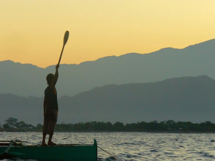 a silhouette of a person standing in a green canoe