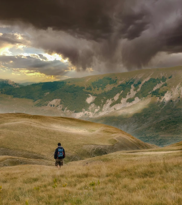 a lone man is looking over the hill to the mountains