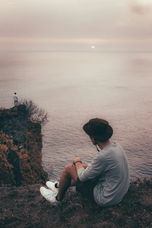 person in straw hat on cliff overlooking ocean and cliffs