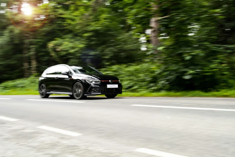 a black car driving along a road next to a forest