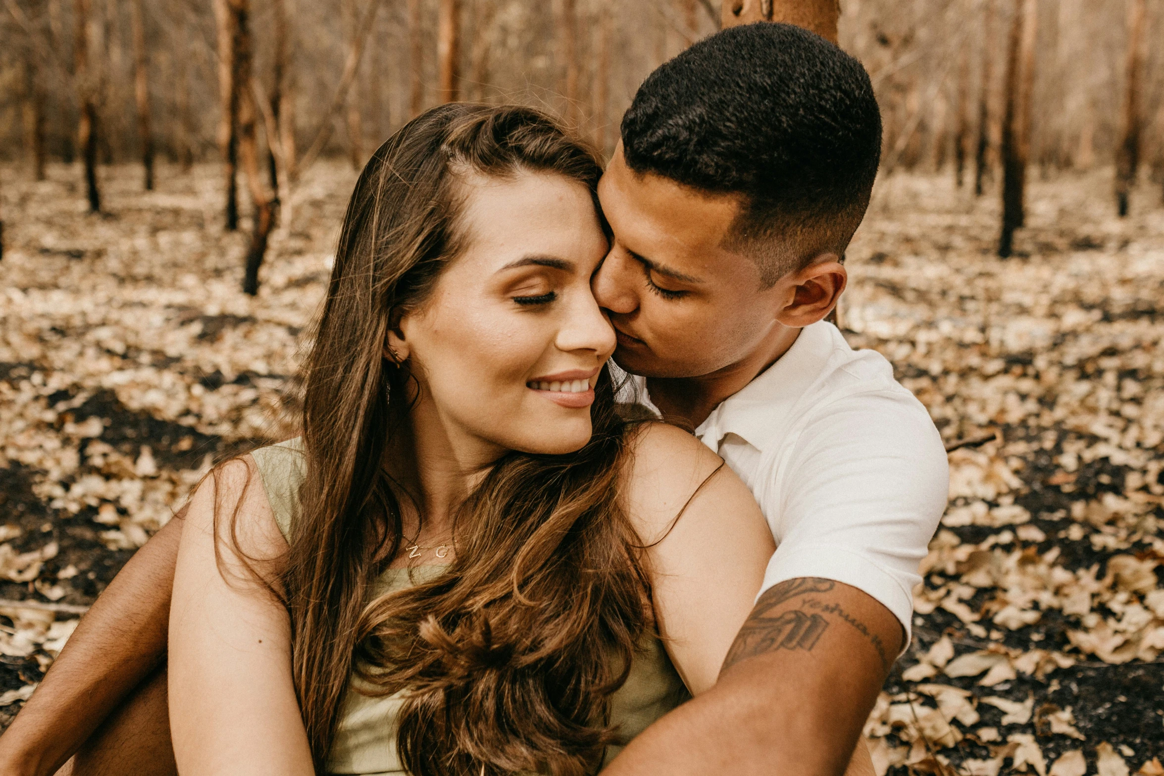 a beautiful young woman hugging a man and holding her cheek in an open field with fallen leaves