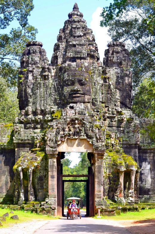 two people riding on a bike in front of an old stone archway