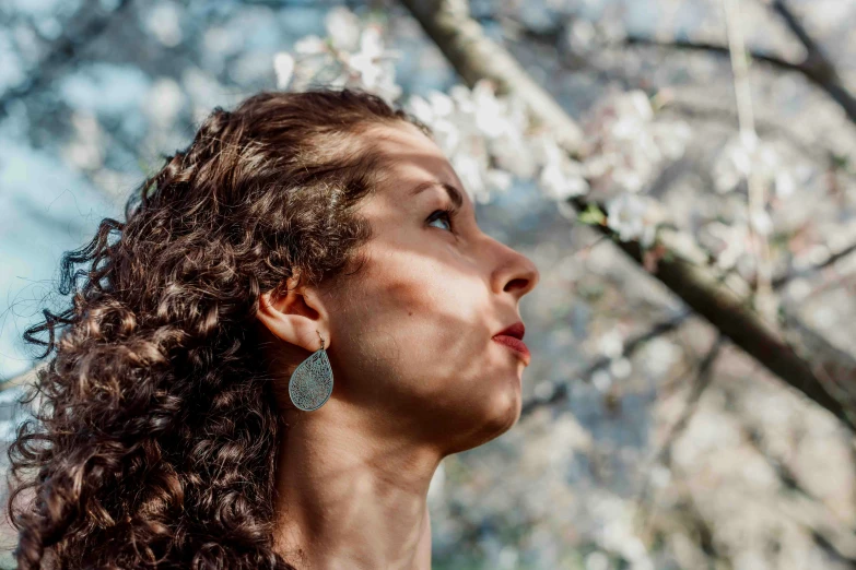 a woman standing in the grass and looking up at a flower