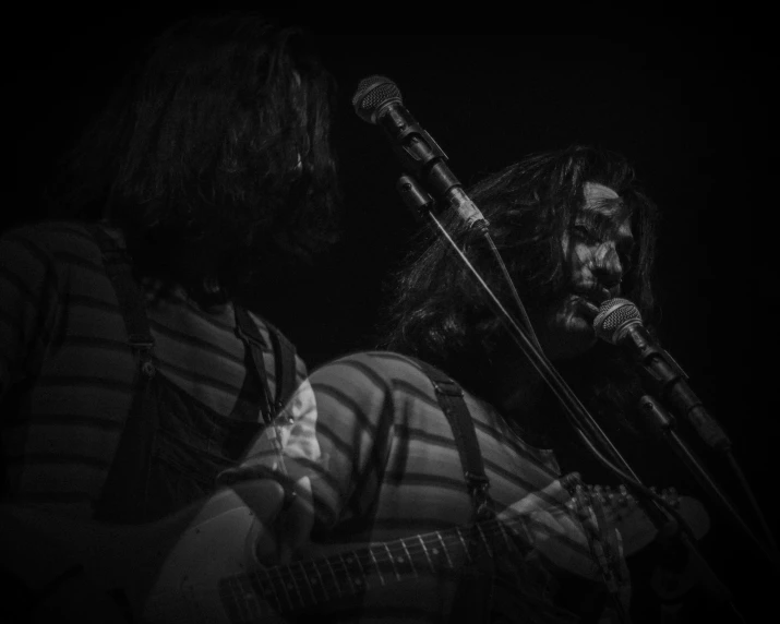 a man in striped shirt sitting next to another person with a guitar