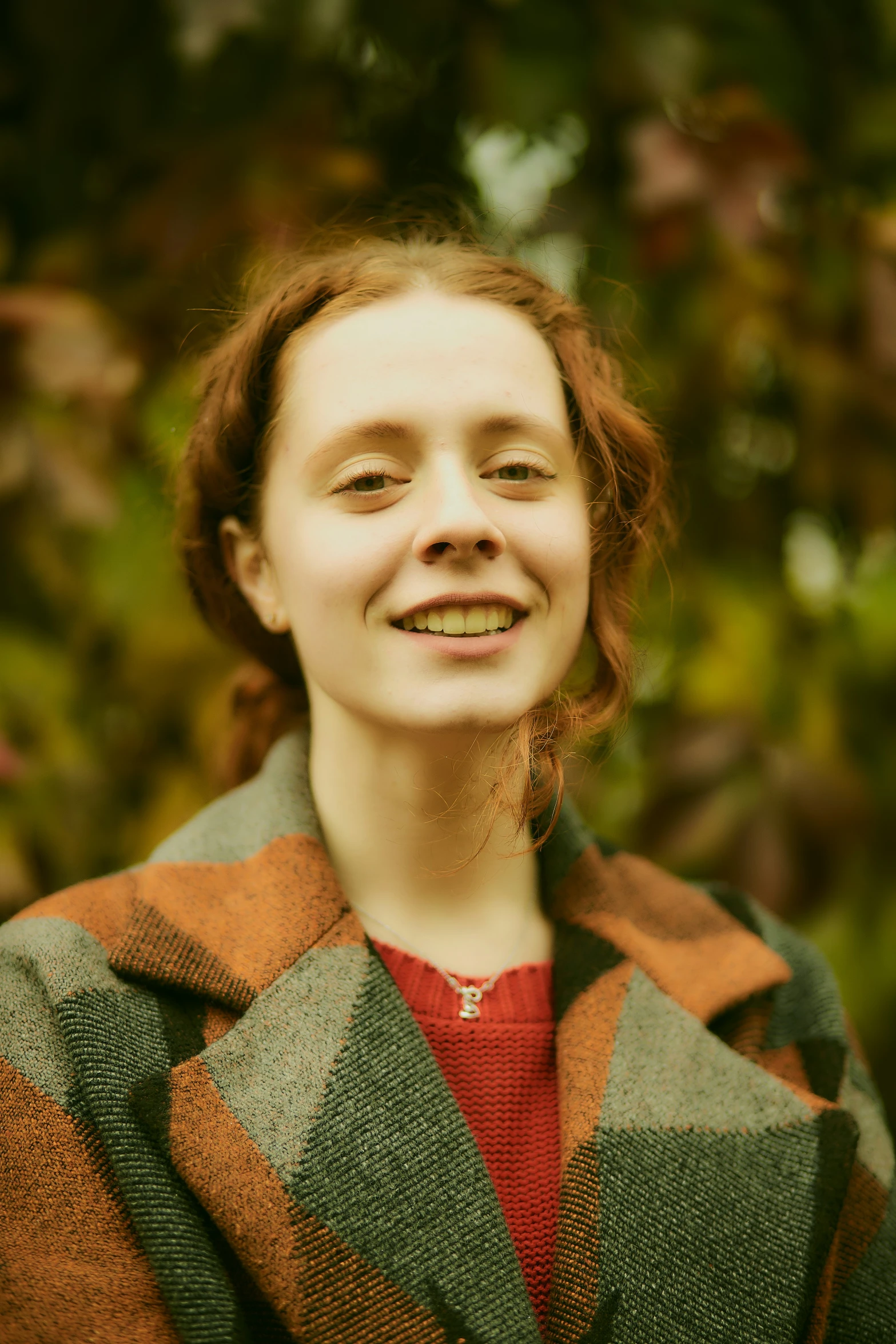 a woman with a multicolored coat stands and smiles at the camera