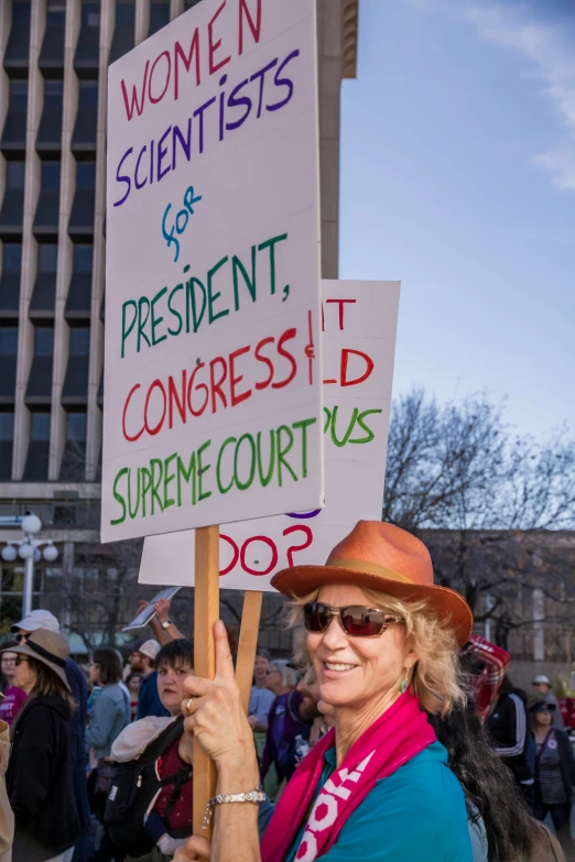 woman holding a sign and a microphone and wearing a hat