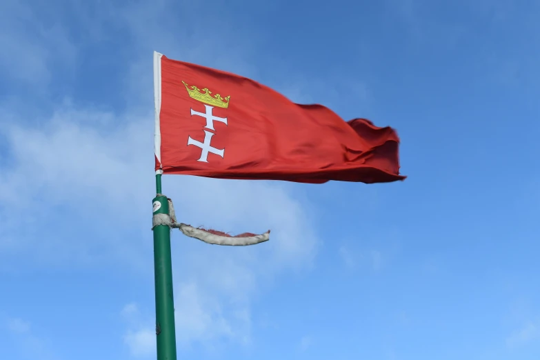a red flag with white and yellow lettering flying in a blue sky