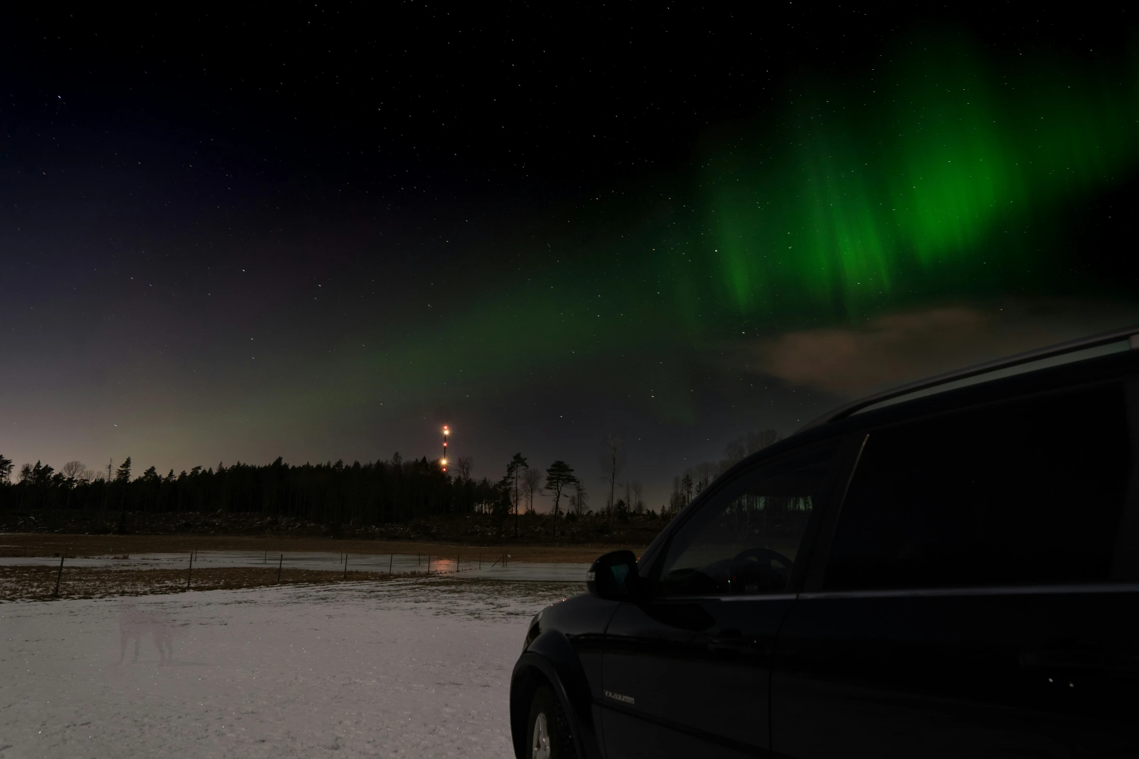 a car is parked in the snow with an aurora light on it