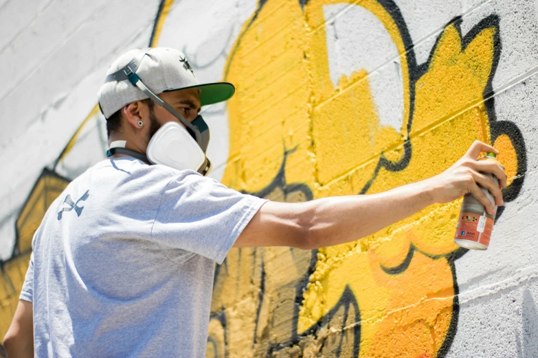 a man in a white cap painting the side of a yellow wall