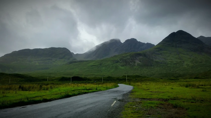 an empty road leading into a field that has some mountains in the background