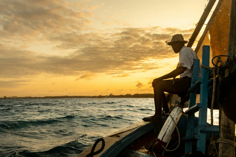 a man sitting on the side of a boat in the ocean at sunset