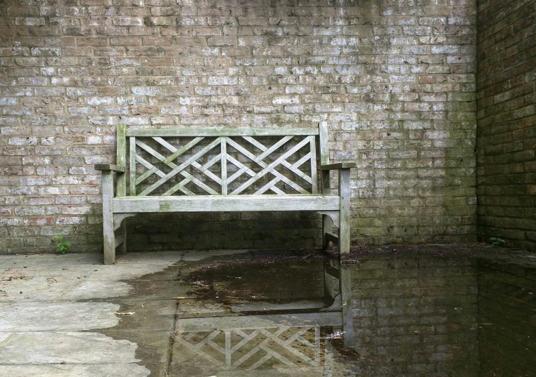 a park bench against a brick wall reflecting water