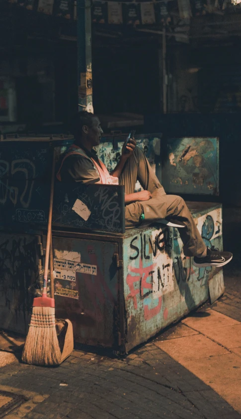 a man laying down on a crate holding a broom and hat