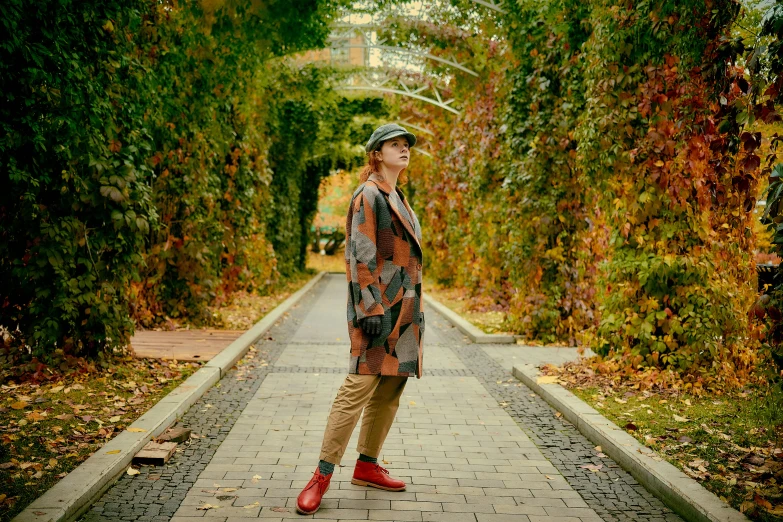 a woman in a hat and cardigan stands in front of a pathway lined with trees