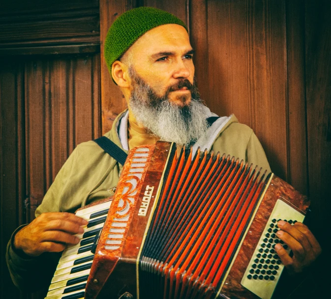 man with beard holding an accordion in front of a wall