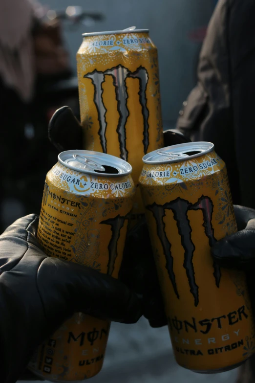 a person is holding three yellow monster energy drinks