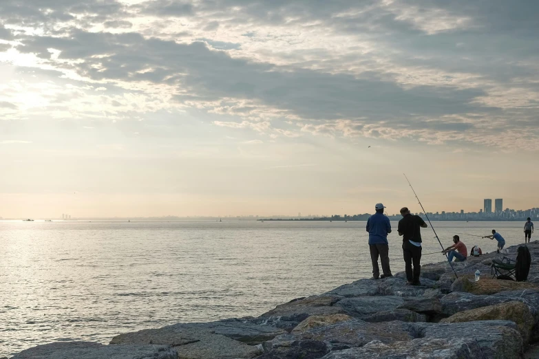 three people standing on rocks next to the water at dusk