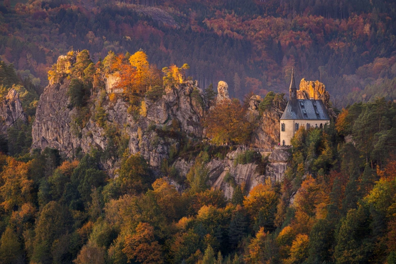 an old church at the top of a mountain with autumn foliage around