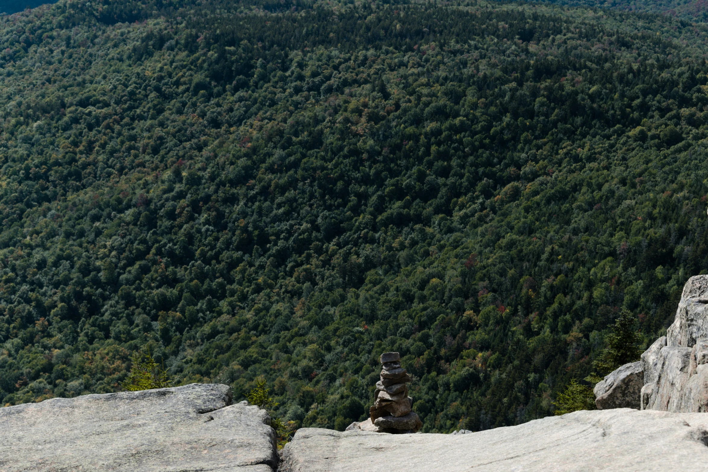 three stacked rocks with trees and mountain behind