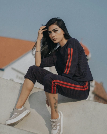 a woman is sitting on the edge of a ledge wearing a track suit