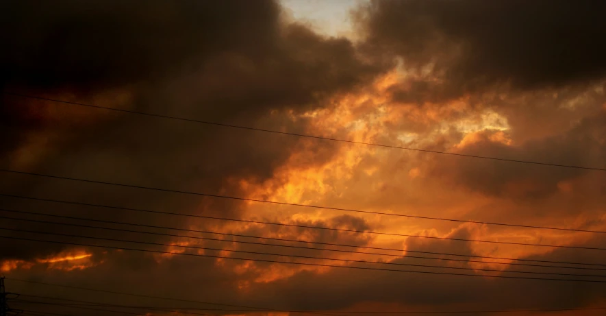 a yellow cloudy sky with the silhouette of wires and telephone poles