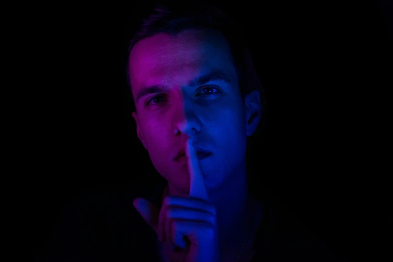 man wearing dark clothes points finger at his mouth